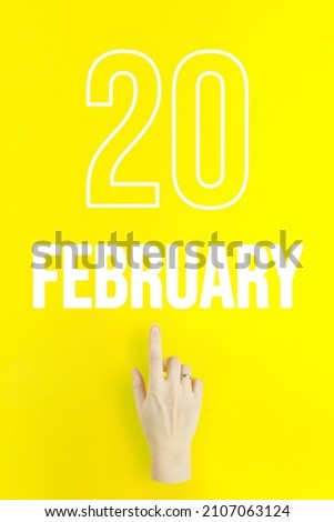 February 20th. Day 20 of month, Calendar date.Hand finger pointing at a calendar date on yellow background.Winter month, day of the year concept
