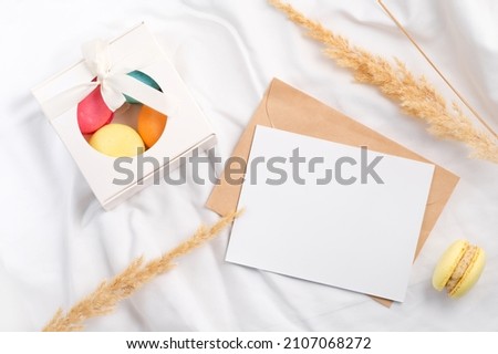 Colorful macarons in box and mockup letter with dry grass on white textile, St. Valentines day concept