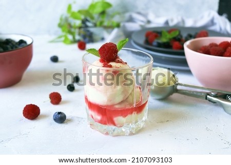 Fresh raspberries and blueberries, creamy ice cream poured with fruit syrup, light background, healthy food, natural dessert, home cooking 