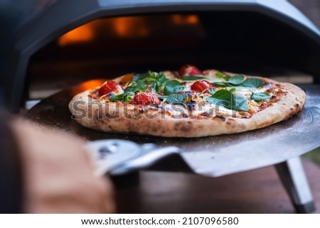 A pizza margarita with fresh basil leaves on the background of a gas oven for cooking pizza. Royalty-Free Stock Photo #2107096580