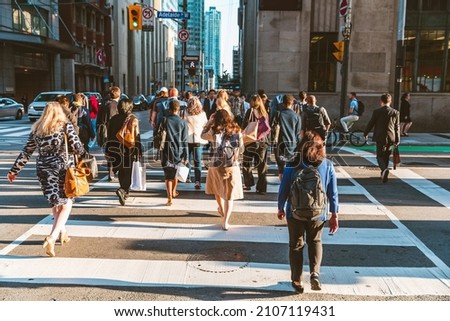 Crowd of unrecognisable people crossing street on traffic light zebra in the city of Toronto at rush hour - Lifestyle in a big city in North America Royalty-Free Stock Photo #2107119431