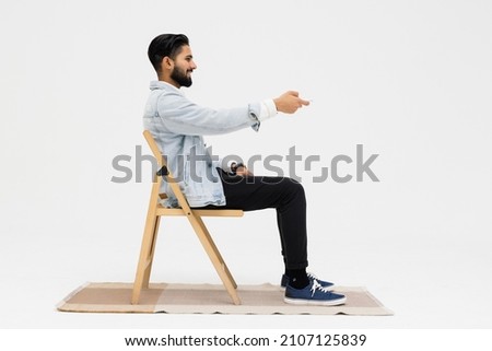 Side view of Asian man sitting in the armchair while watching TV in the studio Royalty-Free Stock Photo #2107125839