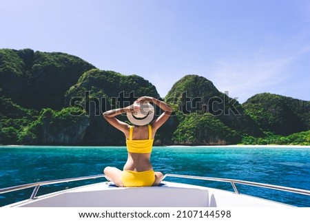 Rear view of adult traveling woman sit and relax on the sailing boat wear yellow bikini blue sky and sea. Summer vacation island domestic trip at Maya bay. Krabi, Thailand Royalty-Free Stock Photo #2107144598