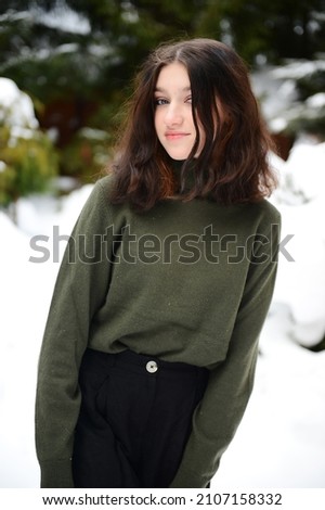 Portrait of beauty brunette teen age girl in dark green sweater and black trousers posing for photos having fun on snowy day