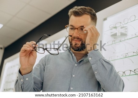 Young man choosing spectacles at optic shop Royalty-Free Stock Photo #2107163162