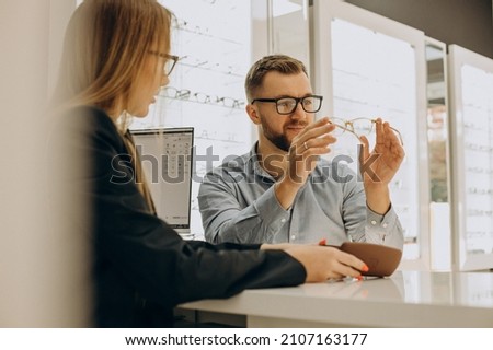 Customer shoosing spectacles at optic store with the lelp of sales person Royalty-Free Stock Photo #2107163177