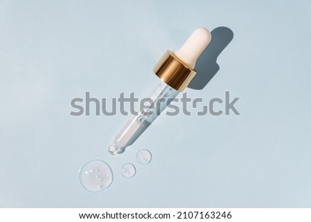 Pink beauty face oil dripping from gold dropper on blue background. Skin care cosmetic advertisement with copy space Royalty-Free Stock Photo #2107163246