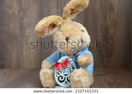 Easter bunny holding a beautiful Easter egg, white egg, Easter picture, bunny on a brown background
