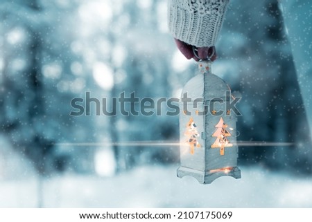 Girl holds in hands a white Christmas lantern with a lamp,walking in the snowy forest during a cold evening,Bethlehem light shines in the dark forest,Christmas atmosphere, christmas is coming 2021