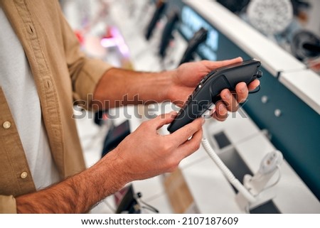 A bearded stylish man makes a choice while standing at a showcase with electronic trimmers and razors. Buying a new trimmer in the store. Royalty-Free Stock Photo #2107187609