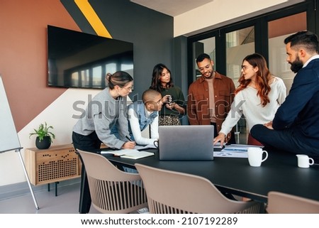Diverse businesspeople discussing some reports in a boardroom. Group of multicultural businesspeople standing around a table in a modern office. Young entrepreneurs collaborating on a project. Royalty-Free Stock Photo #2107192289