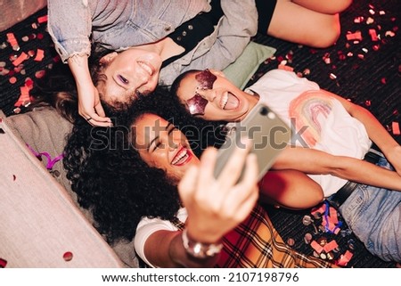 Taking crazy overhead selfies. Top view of three happy friends taking a selfie while lying on the floor at a house party. Group of cheerful female friends having fun together on the weekend.
