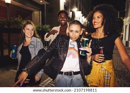 Group of happy friends dancing in the city at night. Four vibrant young people holding beer cans while walking together in the street. Friends having a good time on a weekend night. Royalty-Free Stock Photo #2107198811