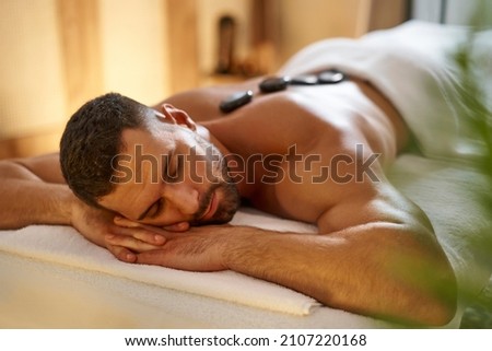 Young man having a hot stone lastone massage at spa Royalty-Free Stock Photo #2107220168