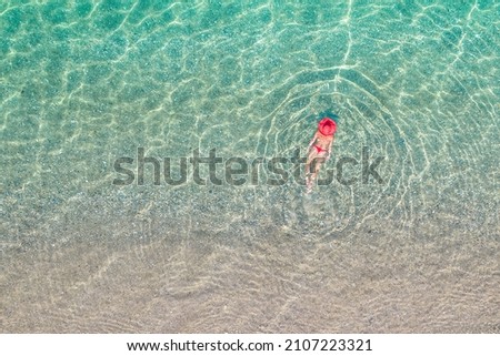 Top view. Young beautiful woman in a red hat and bikini swimming in sea water on the sand beach. Drone, copter photo. Summer vacation. View from above. 