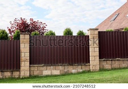 Brown metal profile fence with block posts. Incline construction. Corrugated surface. Security. Private property fencing. Opaque hedge. Outdoor house exterior. Side view. Urban or industrial style. Royalty-Free Stock Photo #2107248512