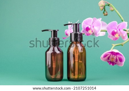 Cosmetic bottles with dispensers on a green background with orchid flowers