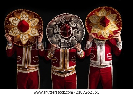Mexican mariachi musicians cover their faces with a sombrero on a black background