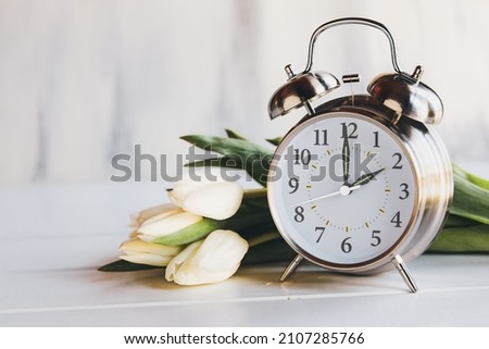 Daylight savings time concept. Set your clocks and to 2 am with this image of an alarm clock with white tulip flowers. Selective focus with blurred foreground and background with copy space. Royalty-Free Stock Photo #2107285766