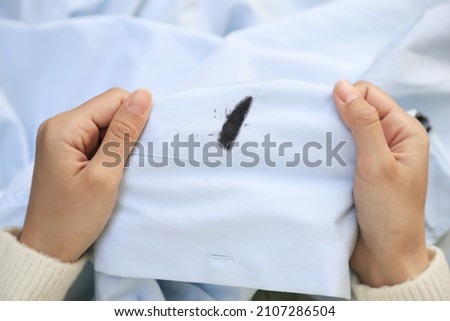 Hand showing dirty black ink stain on white shirt from unexpected accident. daily life stain concept.