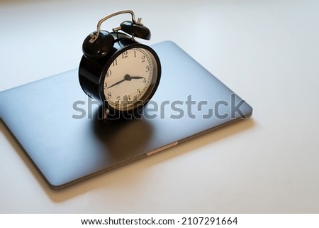 Alarm clock standing on laptop. Concept of work hours, deadline and limit screen time. Royalty-Free Stock Photo #2107291664