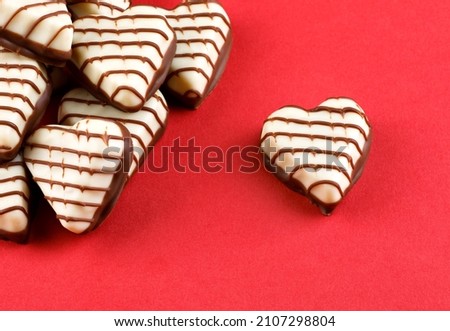 A bunch of heart - shaped chocolates on a red background . One candy heart lies apart from the others .