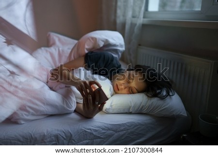Social media jealousy. Young depressed woman addicted to mobile phone lying in bed at home, scrolling social media, feeling envious of lives of others, reading what people posting and sharing online Royalty-Free Stock Photo #2107300844
