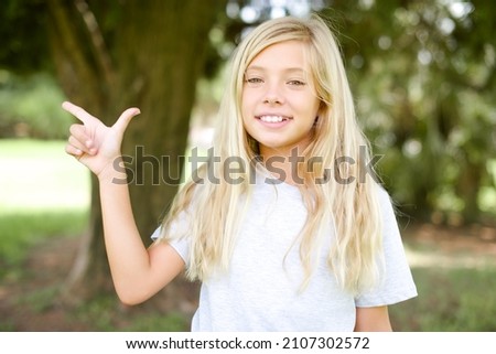 caucasian little kid girl wearing t-shirt standing outdoors pointing up with fingers number eight in Chinese sign language BÄ.