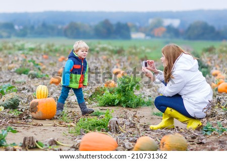 Young mother making picture on mobile phone of her child on pumpkin patch