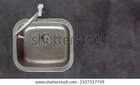 Tap water pours into the steel sink in the kitchen. Top view. Royalty-Free Stock Photo #2107317749