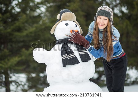 Winter fun, happy young woman playing with snowman