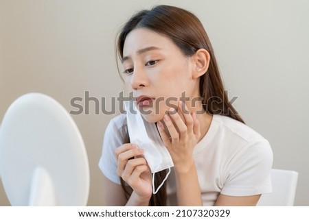 Dermatology, puberty asian young woman, girl looking into mirror, allergy when wear mask and cosmetic, show squeezing pimple spot for removing from face.Beauty care from skin problem by acne treatment Royalty-Free Stock Photo #2107320329