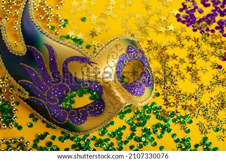 Mardi Gras gold color beads with Luxury Masquerade venetian festival carnival mask and golden, green, purple confetti on yellow background. Party invitation, greeting card for venetian carnivale 