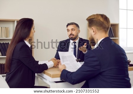 Family lawyer in suit speaking to clients. Couple sitting at desk, reading divorce settlement agreement, consulting with law expert, listening to him answer questions, and getting help with paperwork Royalty-Free Stock Photo #2107331552