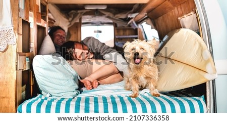 Hippie couple with cute pet traveling together on vintage retro campervan - Wanderlust and life inspiration concept with hippie lovers on mini van adventure journey on the road - Bright warm filter Royalty-Free Stock Photo #2107336358