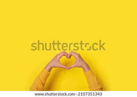 Hands making heart shape, love symbol over yellow background Royalty-Free Stock Photo #2107351343