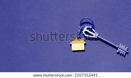 Key chain in the shape of wooden house with key on a purple background. Very peri tinting. Building, design, project, moving to new home, mortgage, rent and purchase real estate. Copy space