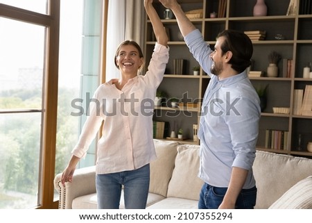 Young lively couple standing in cozy living room holding hands dancing to the favourite music, spend romantic weekend together at fashionable home. Love, celebrate relocation to new own house concept Royalty-Free Stock Photo #2107355294