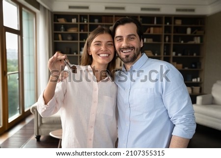 Beautiful homeowners couple, 30s wife and husband hugging pose in fashionable living room holding keys bunch feeling happy at relocation day. Bank loan, real-estate buyers, first home, tenancy concept Royalty-Free Stock Photo #2107355315