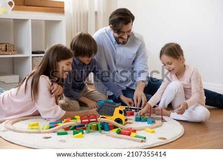 Couple and children spend time together sit on warm floor with underfloor heat enjoy playtime playing wooden railroad and colorful bricks. Quarantine leisure of family with kids, toys store ad concept Royalty-Free Stock Photo #2107355414