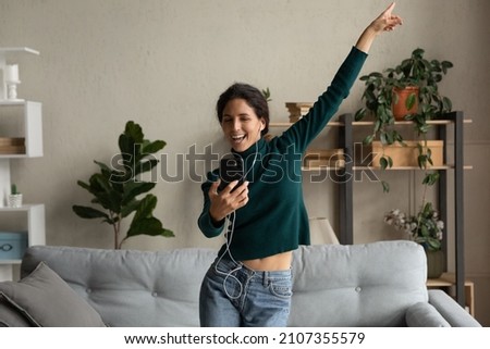 Overjoyed millennial gen beautiful woman dancing, learning moves from educational video on smartphone, recording vlog or having fun choosing audio in modern application, domestic activity concept. Royalty-Free Stock Photo #2107355579