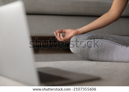 Close up focus on folded female hand lying on knee, cropped young woman in activewear sitting in lotus position, enjoying meditating, breathing fresh air, relaxing after distant yoga workout at home. Royalty-Free Stock Photo #2107355606