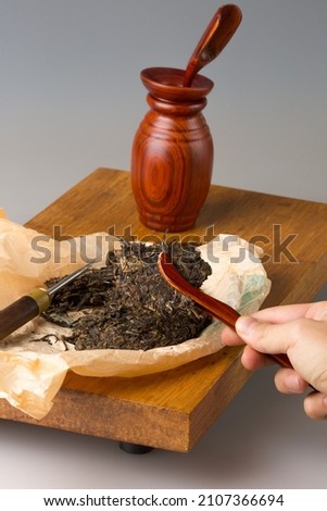 Wooden table for tea ceremonies and a set for brewing tea. Pressed pu-erh tea on the table. A man's hand separates pieces of tea leaves and puts them in a teapot with a spatula.