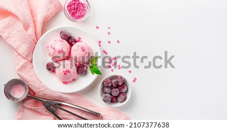 Three ice cream balls with frozen cherries and hearts on a white background. Top view, copy space. Royalty-Free Stock Photo #2107377638