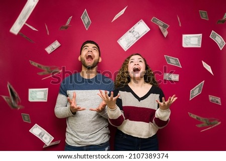 Raining money. Excited young man and woman with a lot of cash feeling very rich after earning their paycheck