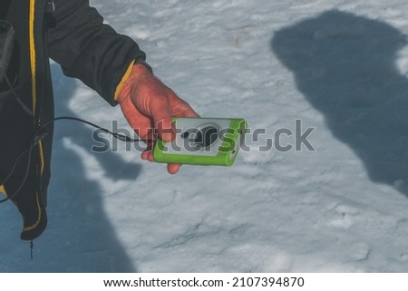 A close-up shot of a Caucasian man's hands holding an avalanche transceiver during a training on avalanche victim rescue Royalty-Free Stock Photo #2107394870