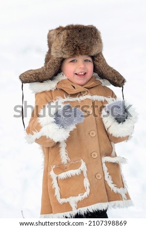 A kid in a winter fur coat, hat and felt boots in a snow-covered forest.A boy in winter Russian folk clothes.Cute blue-eyed boy on a walk in winter.Winter picture like in a fairy tale