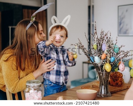 Mother and child draw on Easter eggs and hang them on branches. Preparation of decorations for Easter in the home interior Royalty-Free Stock Photo #2107421480