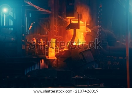 Iron casting in foundry. Metallurgical plant. Liquid metal pouring from ladle container into molds in blast furnace. Heavy metallurgy industry Royalty-Free Stock Photo #2107426019