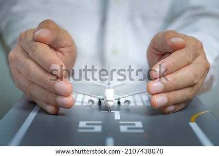 Airplane model on the runway and surrounded by hands. Concept of aviation safety, preventive action, security, and insurance. Royalty-Free Stock Photo #2107438070